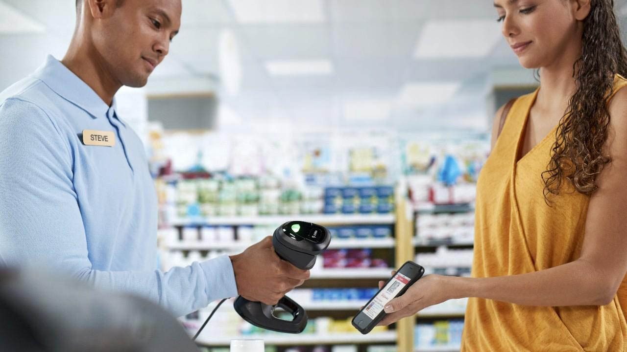 A drug store associate uses a Zebra DS9900 Series barcode scanner to scan a customer`s digital loyalty card barcode